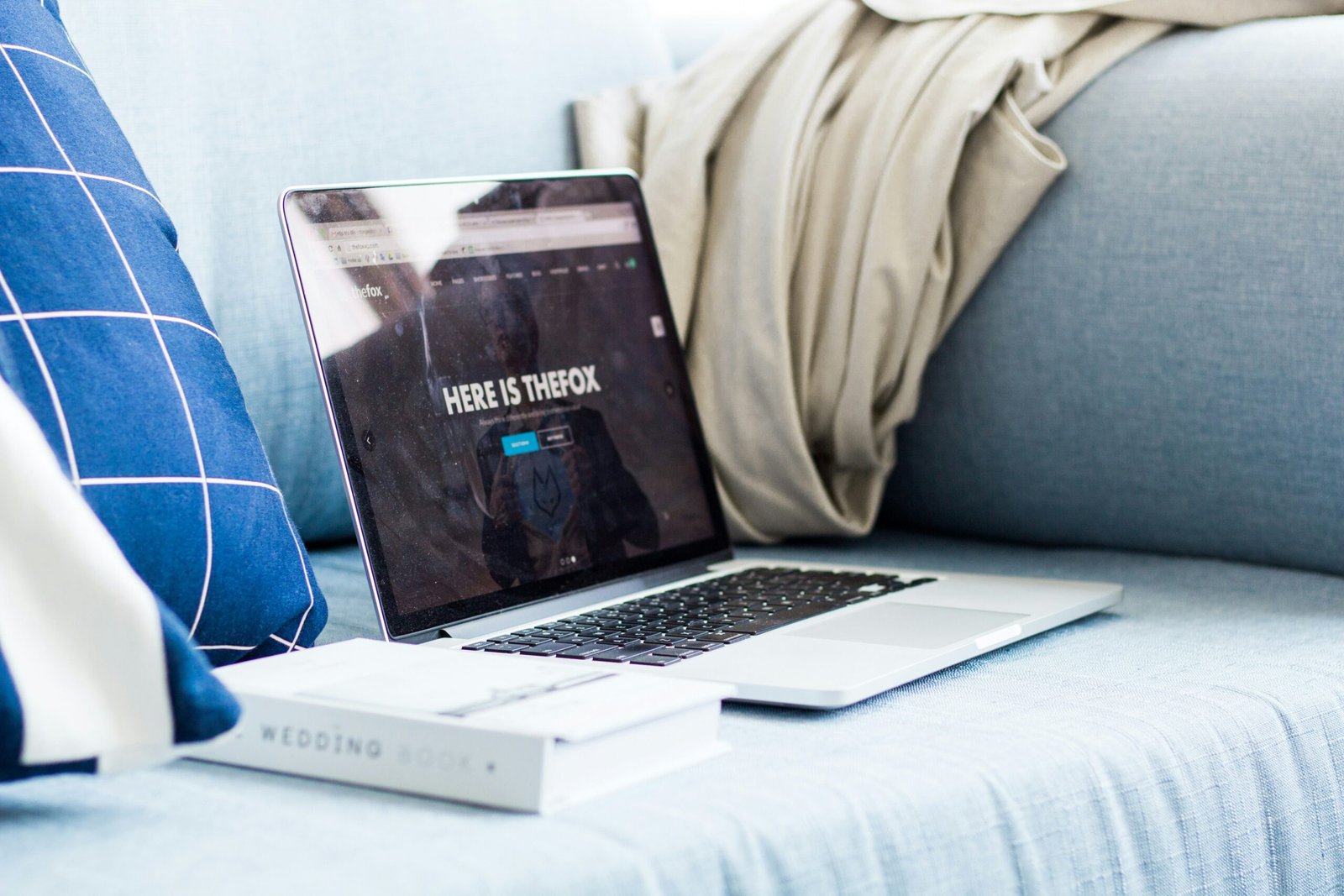 A laptop sitting next to a book on a couch.