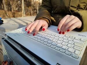 Una mujer con uñas rojas escribiendo en un teclado blanco