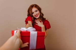 una mujer sosteniendo una caja de regalo roja con una cinta blanca