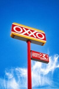 Letrero de la tienda Oxxo iluminado contra un cielo azul.