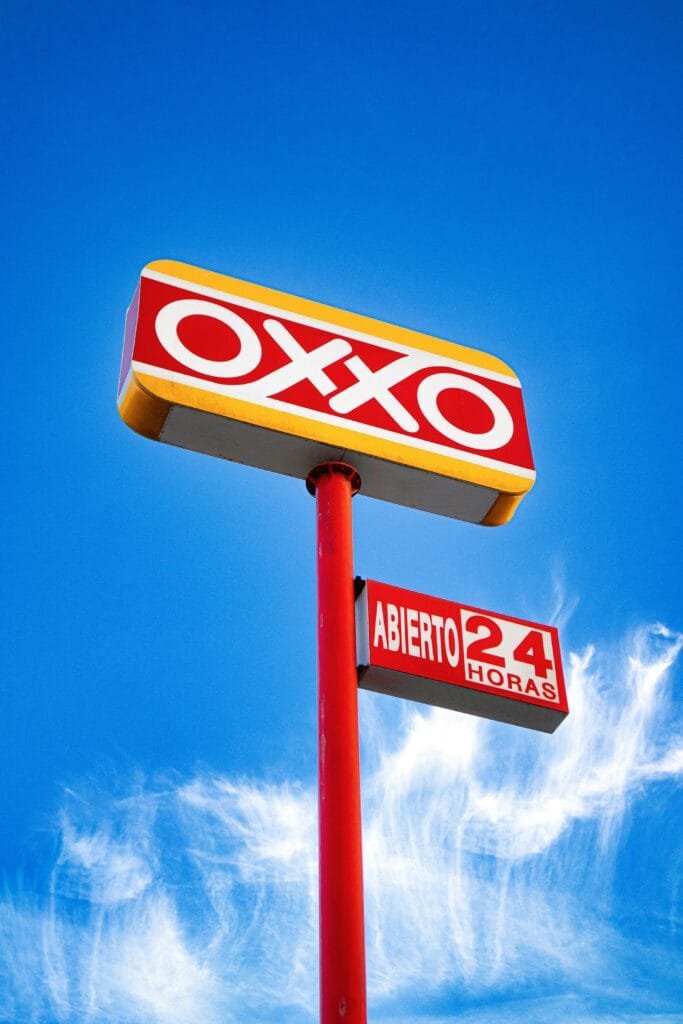Letrero de la tienda Oxxo iluminado contra un cielo azul.